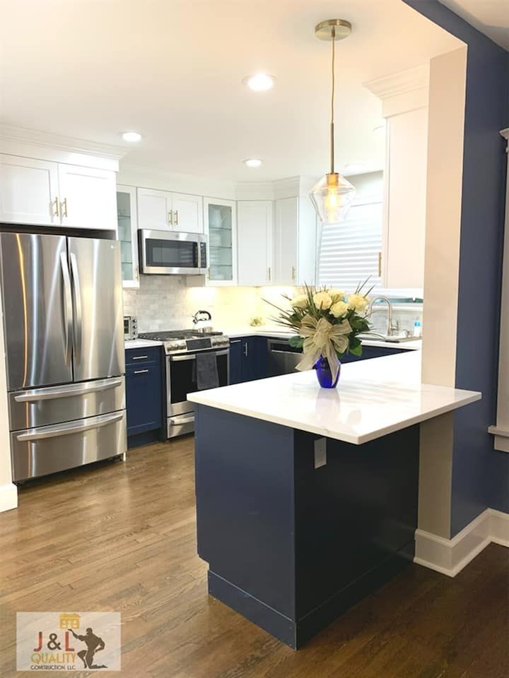 Modern kitchen with white cabinets, stainless steel appliances, and a navy island with a flower vase.
