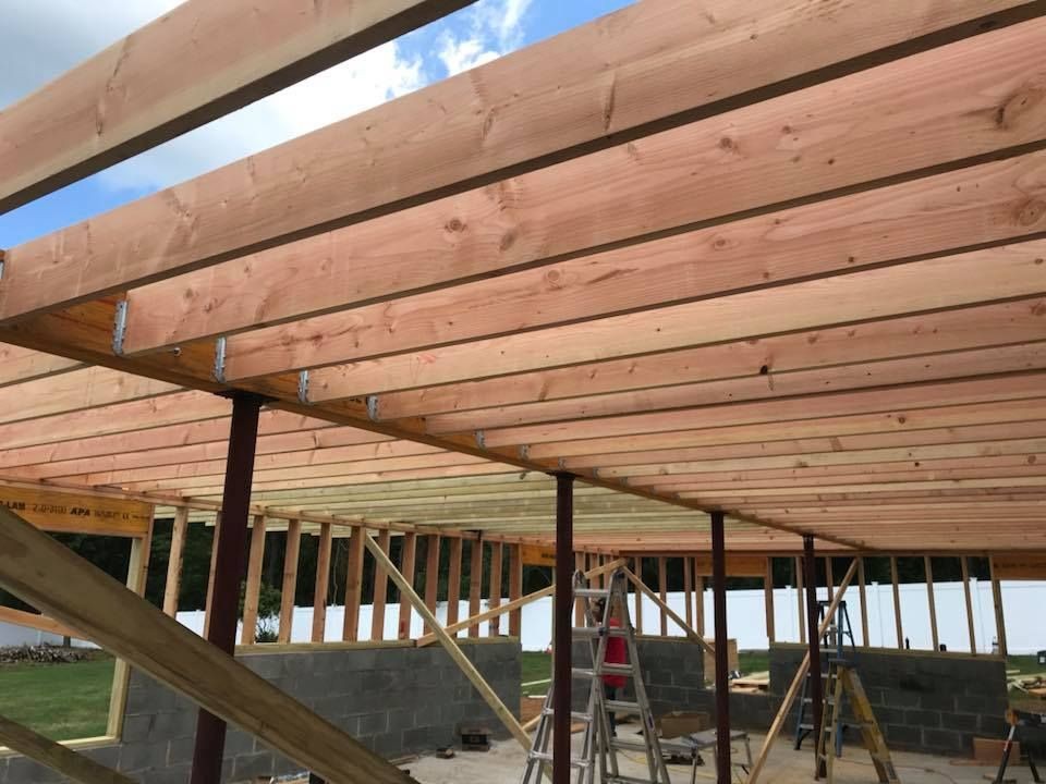 Wooden beams and structure framing a building under construction with ladders and blue sky visible.